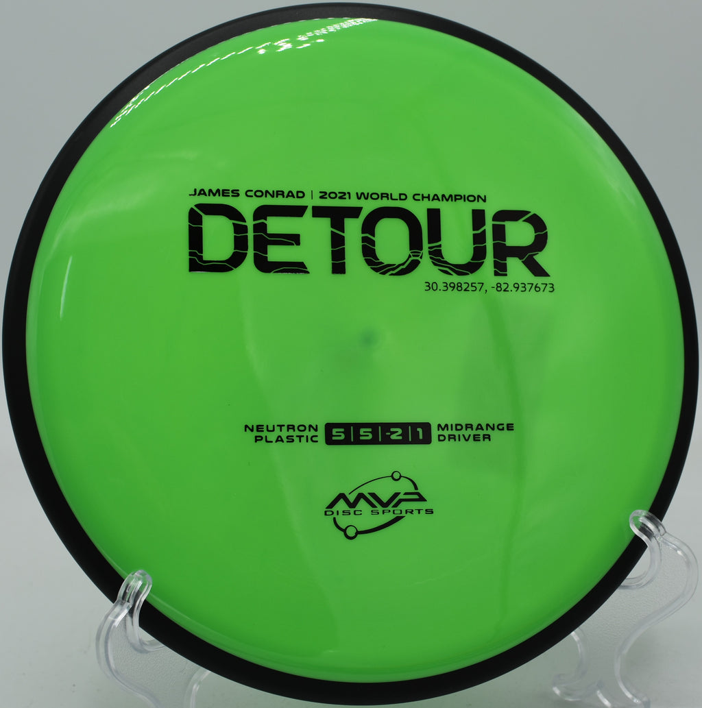 Close-up of Neutron Detour’s stamp and flight plate resting on the tee pad at Ewing Park in Des Moines, Iowa