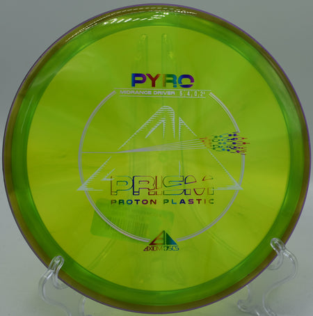 The Prism Proton Pyro disc with bright colors, lying on a grassy field at Idlewild Disc Golf Course in Burlington, Kentucky, showcasing its sleek design and flight stability.