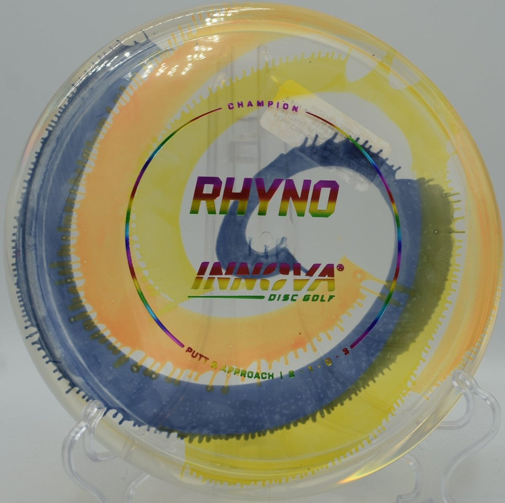 I-Dye Champion Rhyno putter lying beside the basket pole after a controlled hyzer upshot at West Park Disc Golf Course in Joliet, Illinois