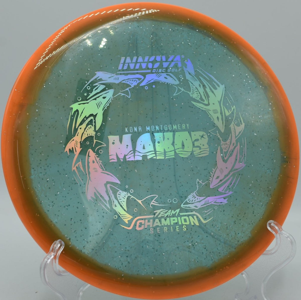 Metalflake Halo Champion Mako3 midrange lying beside the basket pole after a clean hyzer approach at Hunts Hideaway Disc Golf Course in Otisville, Michigan