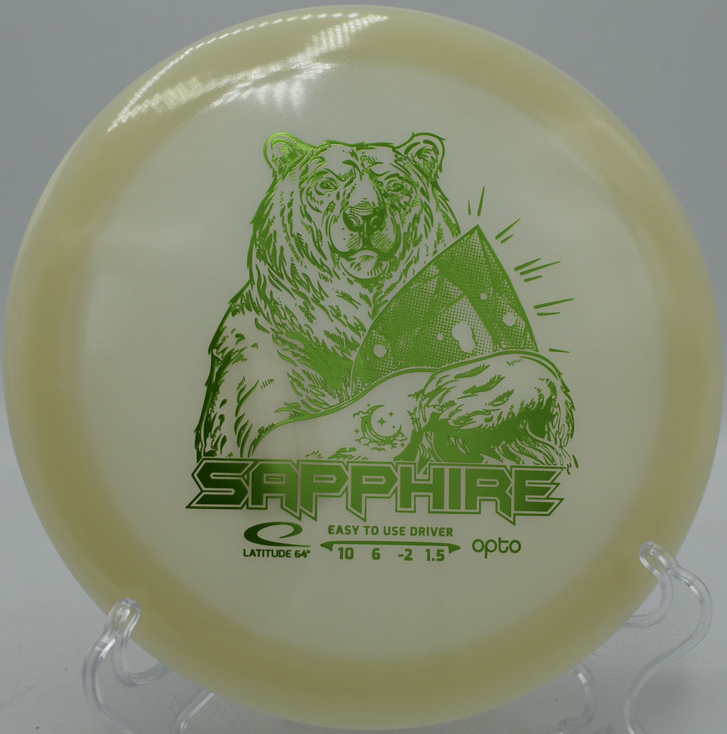 Latitude 64° Opto Moonshine Sapphire glowing lightweight driver soaring on a hyzer-flip at Maple Hill Disc Golf Course in Leicester, Massachusetts.
