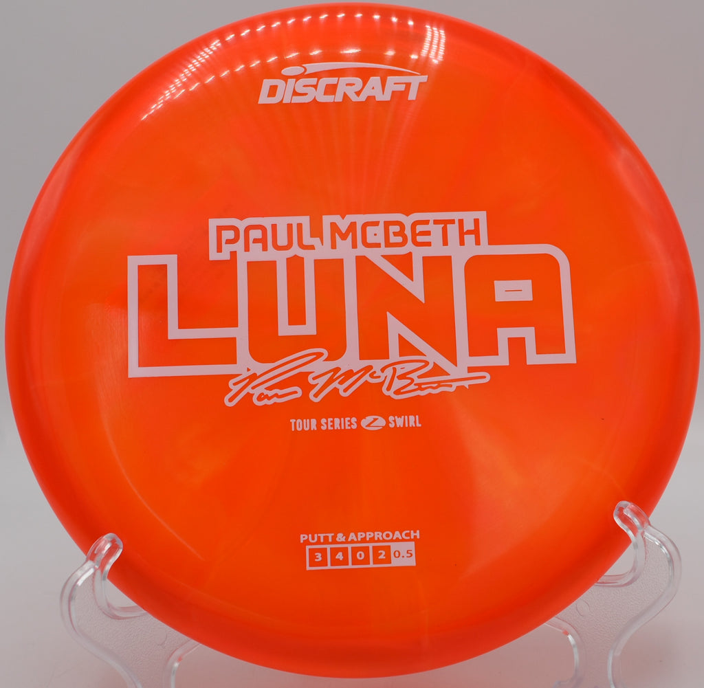 Close-up of the Z Swirl Luna beside the basket at DeLaveaga Disc Golf Course in Santa Cruz, California, highlighting beautiful plastic swirl and beadless design.

