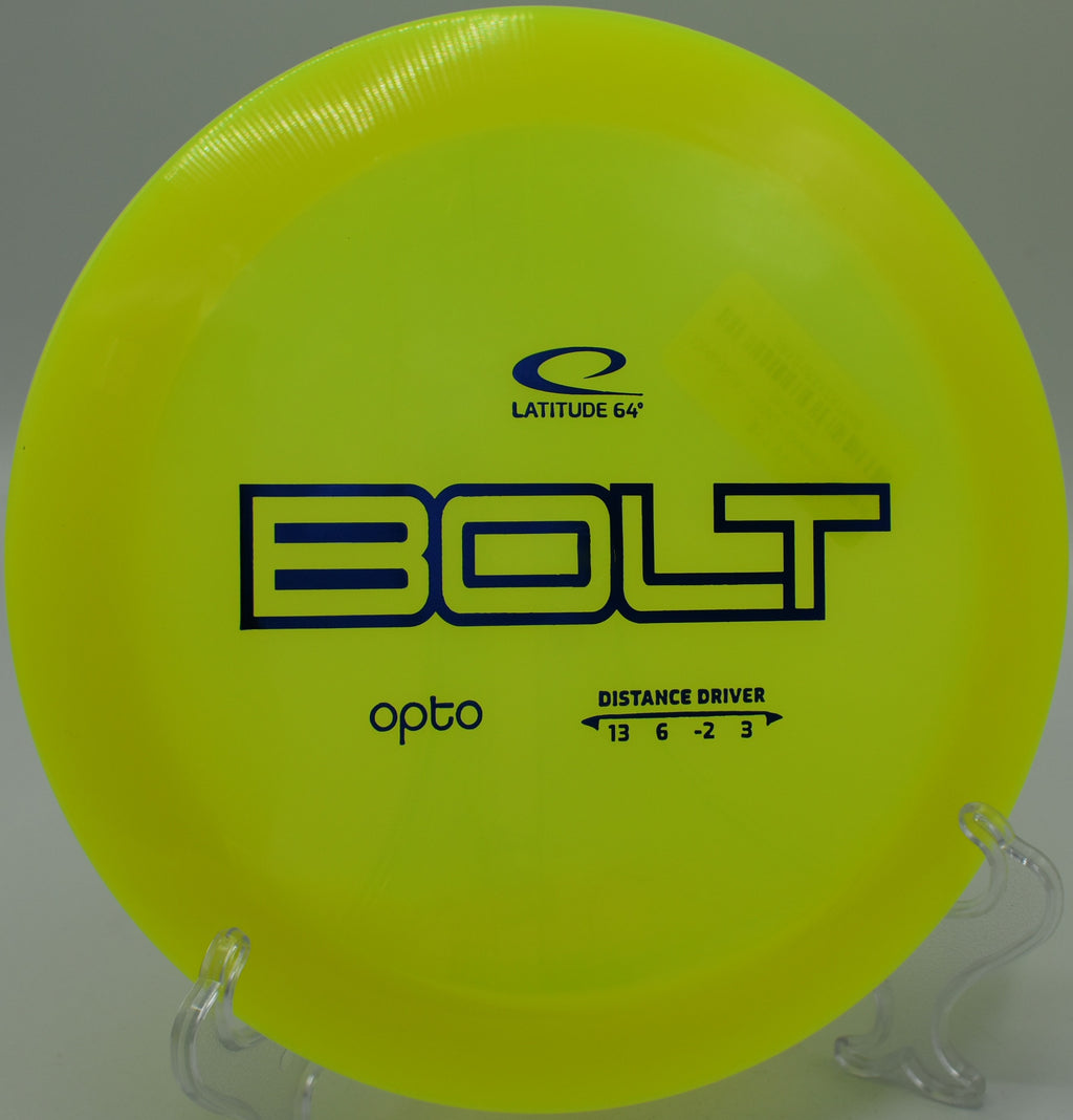Green Opto Bolt disc lying in tall grass near a basket at Misty Hollow Disc Golf Course.