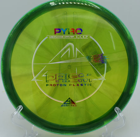 The Prism Proton Pyro disc with a smooth, glossy finish, placed on a wooded tee pad at Maple Hill Disc Golf Course in Leicester, Massachusetts.