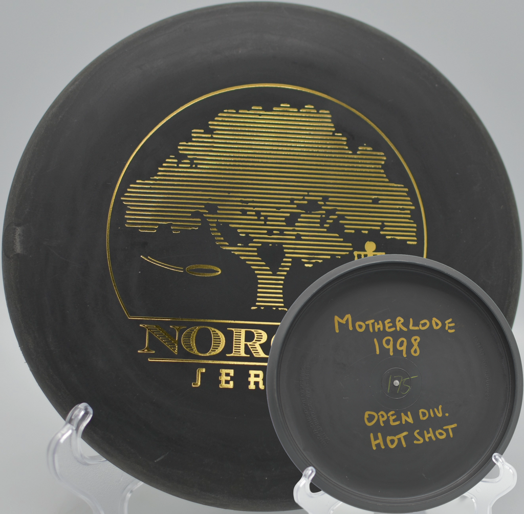 Black 2-Ring San Marino Microbead Aviar w/Pat# (NorCal Series 97–02) parked beside the pin after a smooth putt at Shady Oaks Disc Golf Course in Orangevale, California.